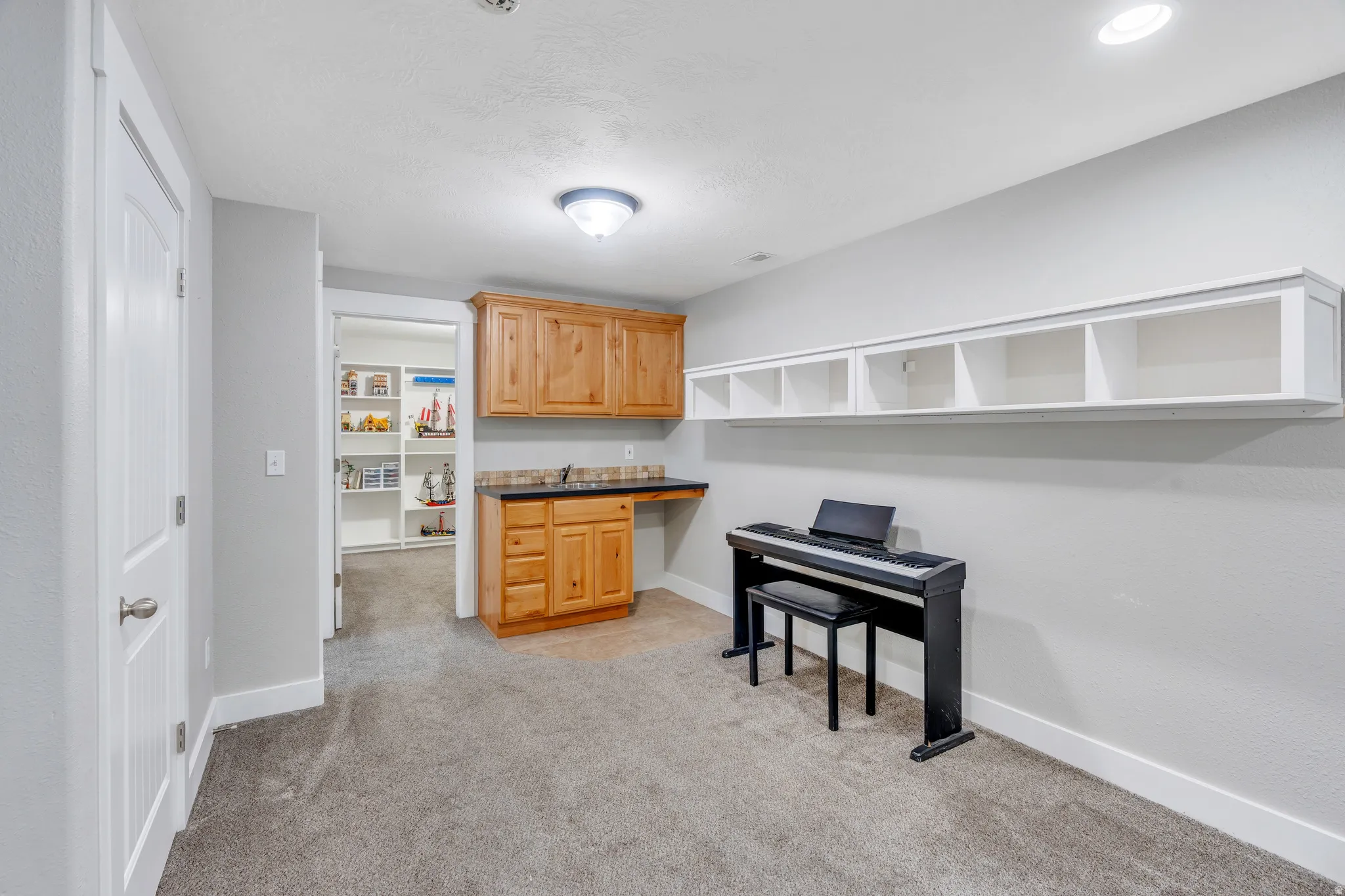 Carpeted room featuring a built-in wood-finish cabinet and countertop area, a wall-mounted shelving unit, and recessed lighting