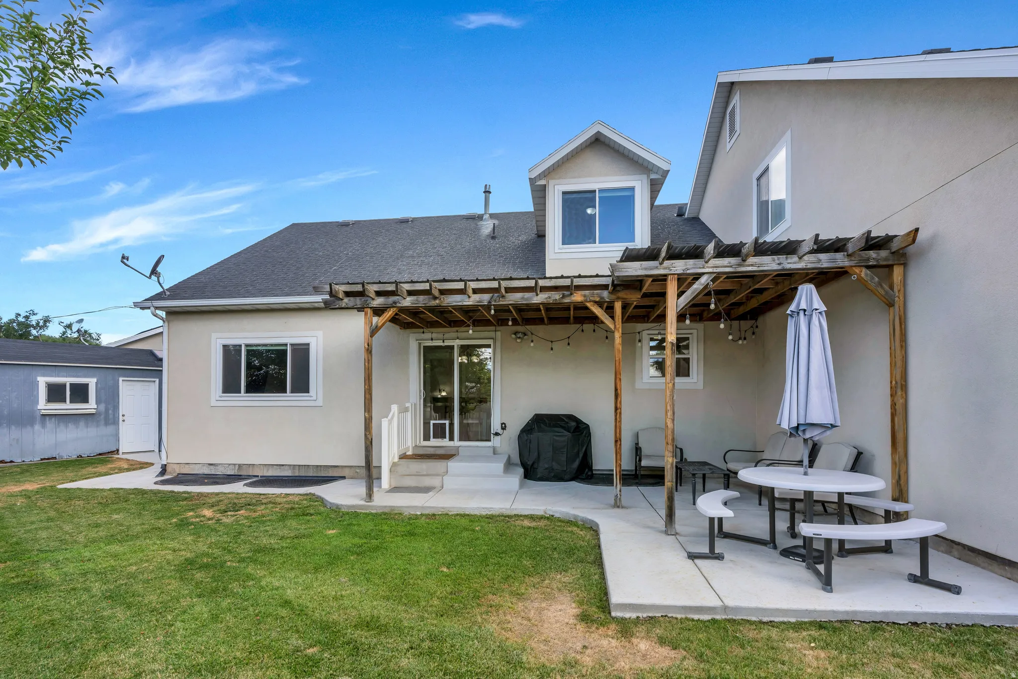 Rear stucco exterior featuring a wood pergola and concrete patio