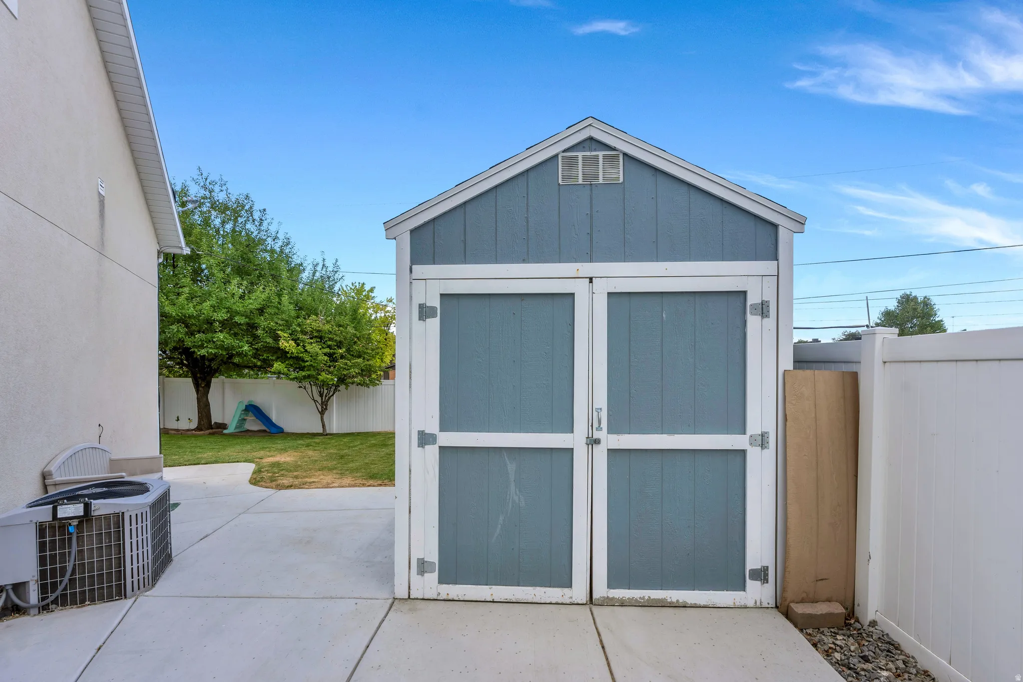 Detached storage shed with blue siding and white trim, featuring double doors and an upper vent