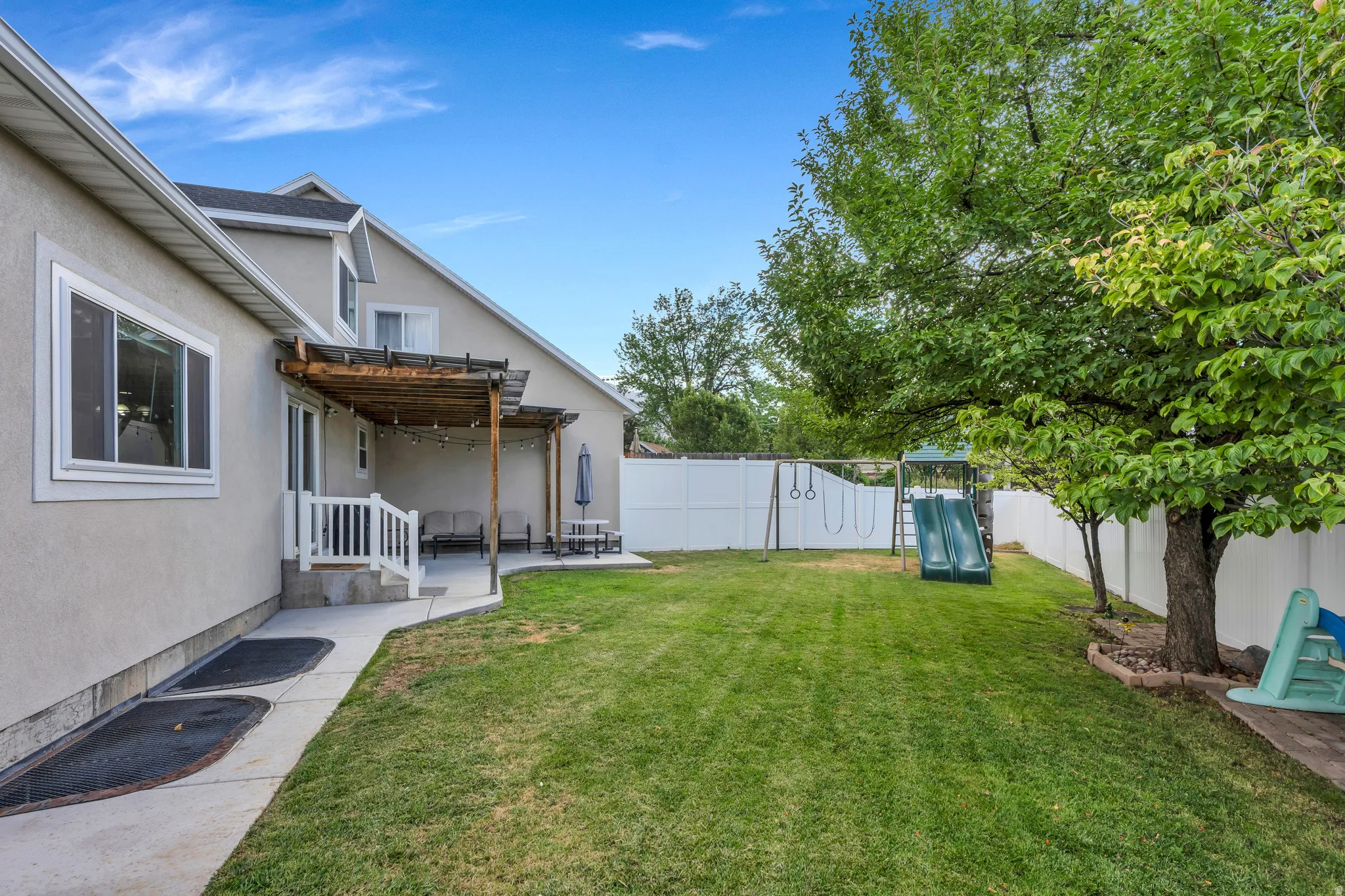 Expansive green lawn with mature trees and a white privacy fence