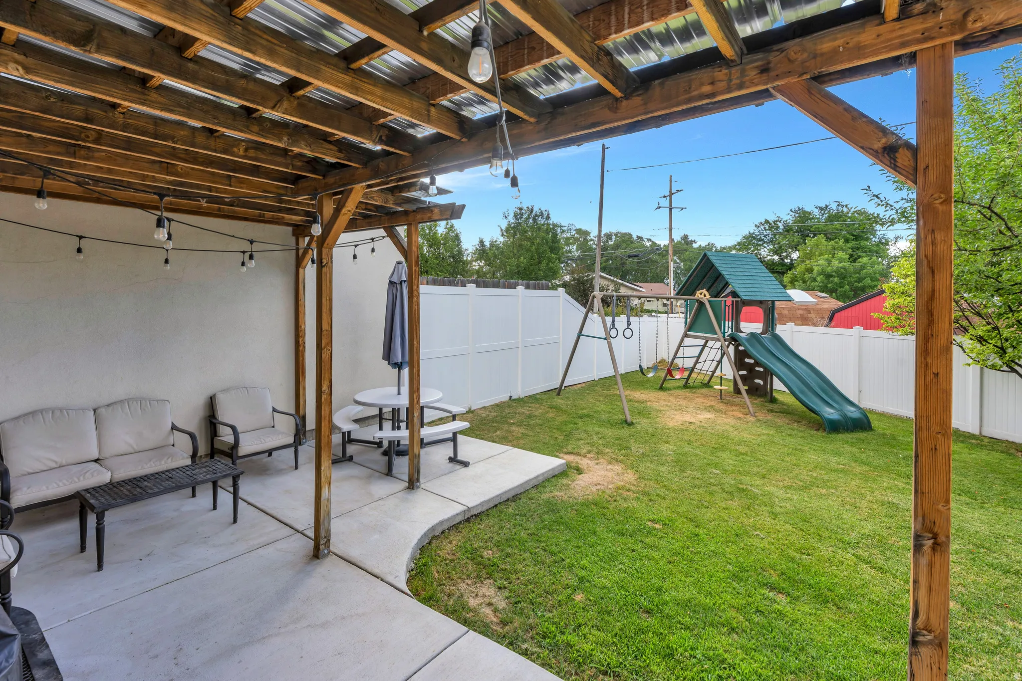 Expansive outdoor patio featuring a wooden pergola with corrugated roofing and string lighting
