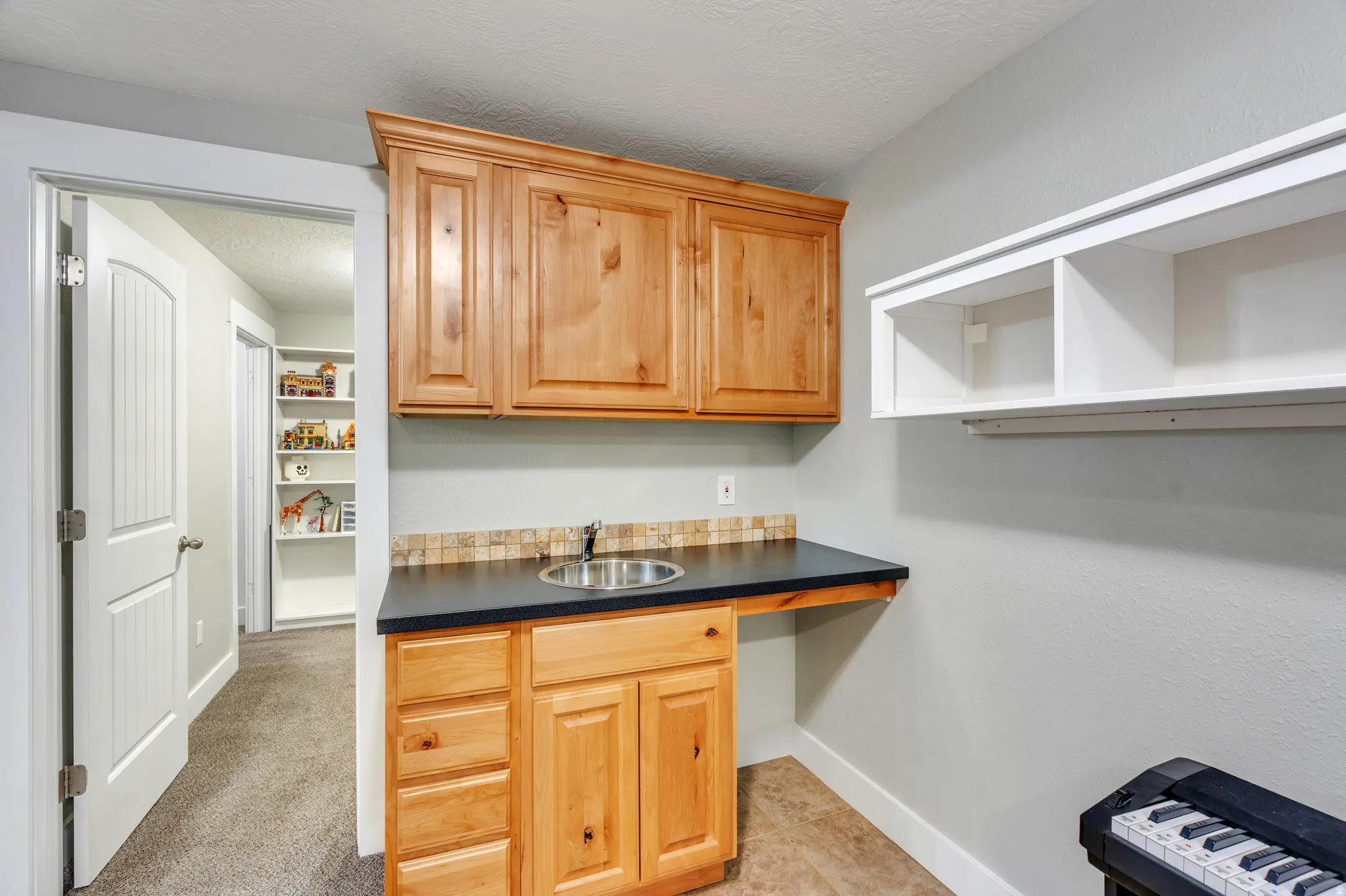 Utility area with a stainless steel sink, wood-finish cabinetry, dark countertop, and a tiled backsplash