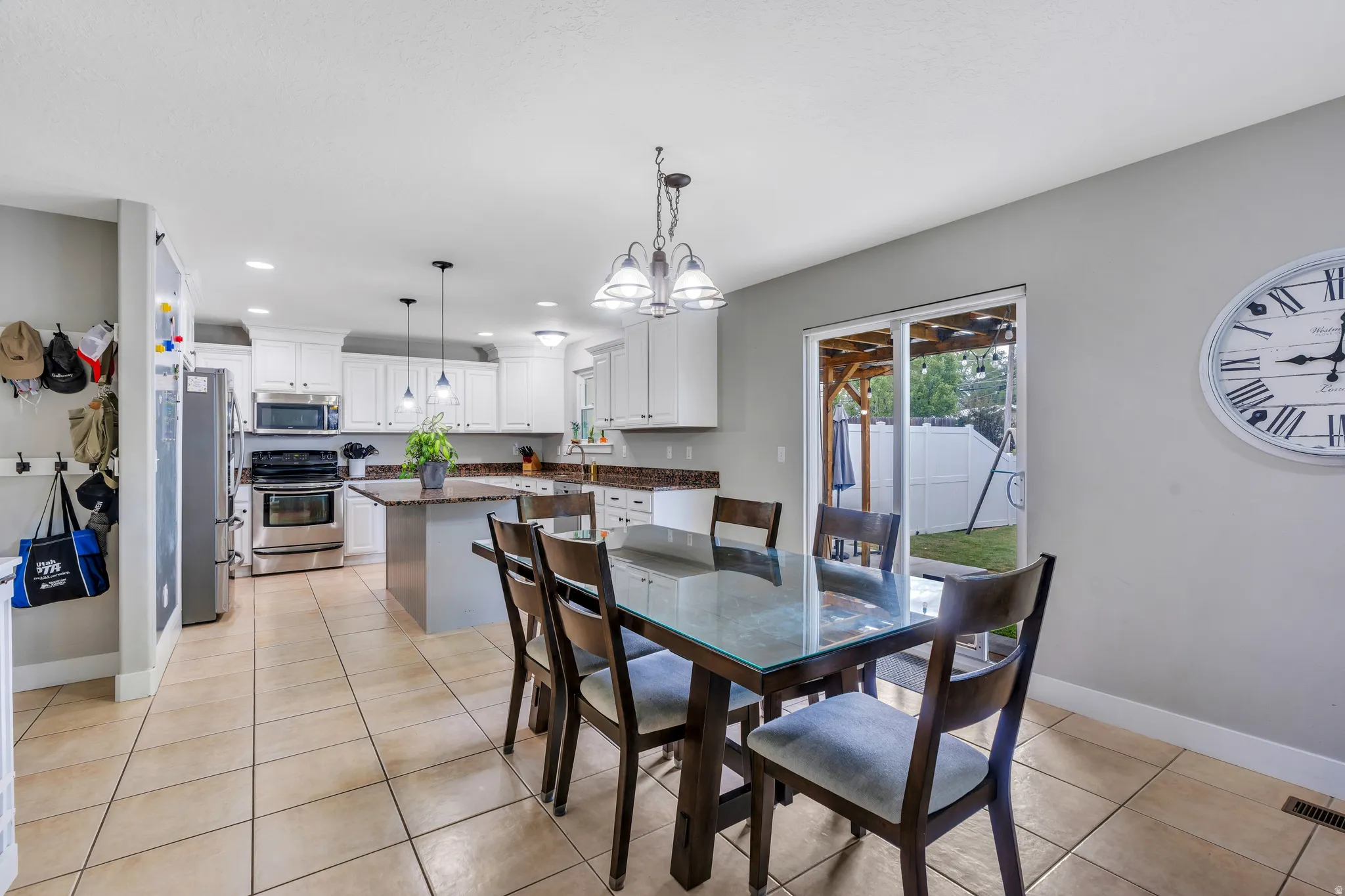 Open-concept kitchen and dining area featuring tile flooring, white cabinetry, a central island with a contrasting base, and stainless steel appliances