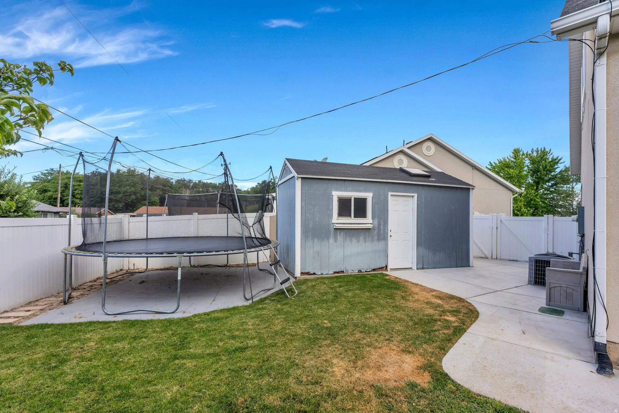 Backyard featuring a gray storage shed with a white door and window, concrete patio, and a grass area
