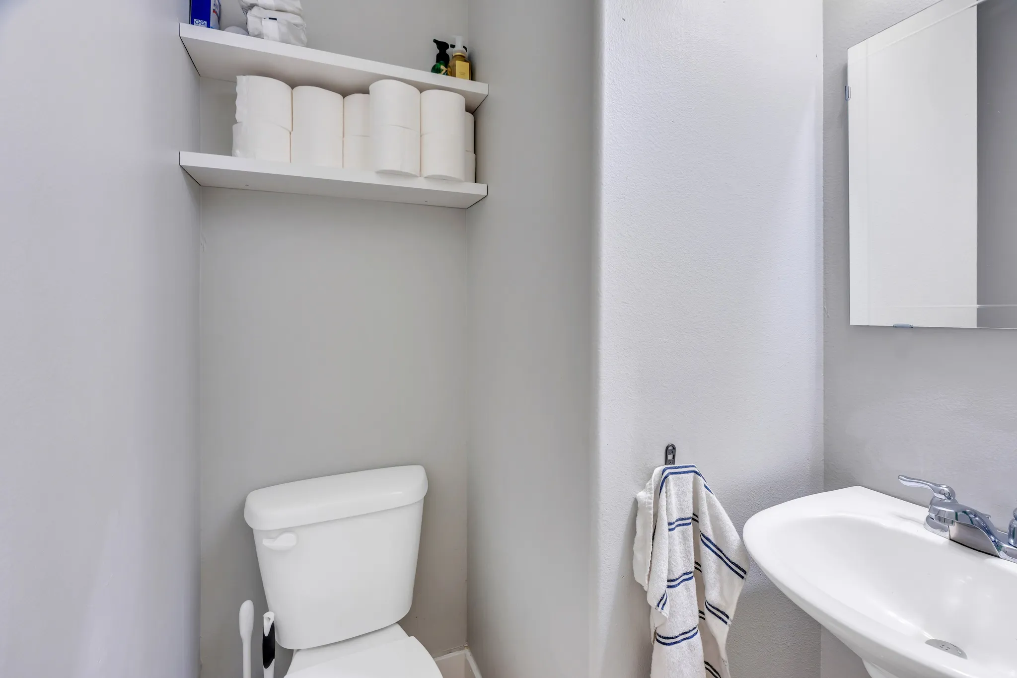 Pedestal sink with chrome fixtures, medicine cabinet, and dual wall-mounted shelving