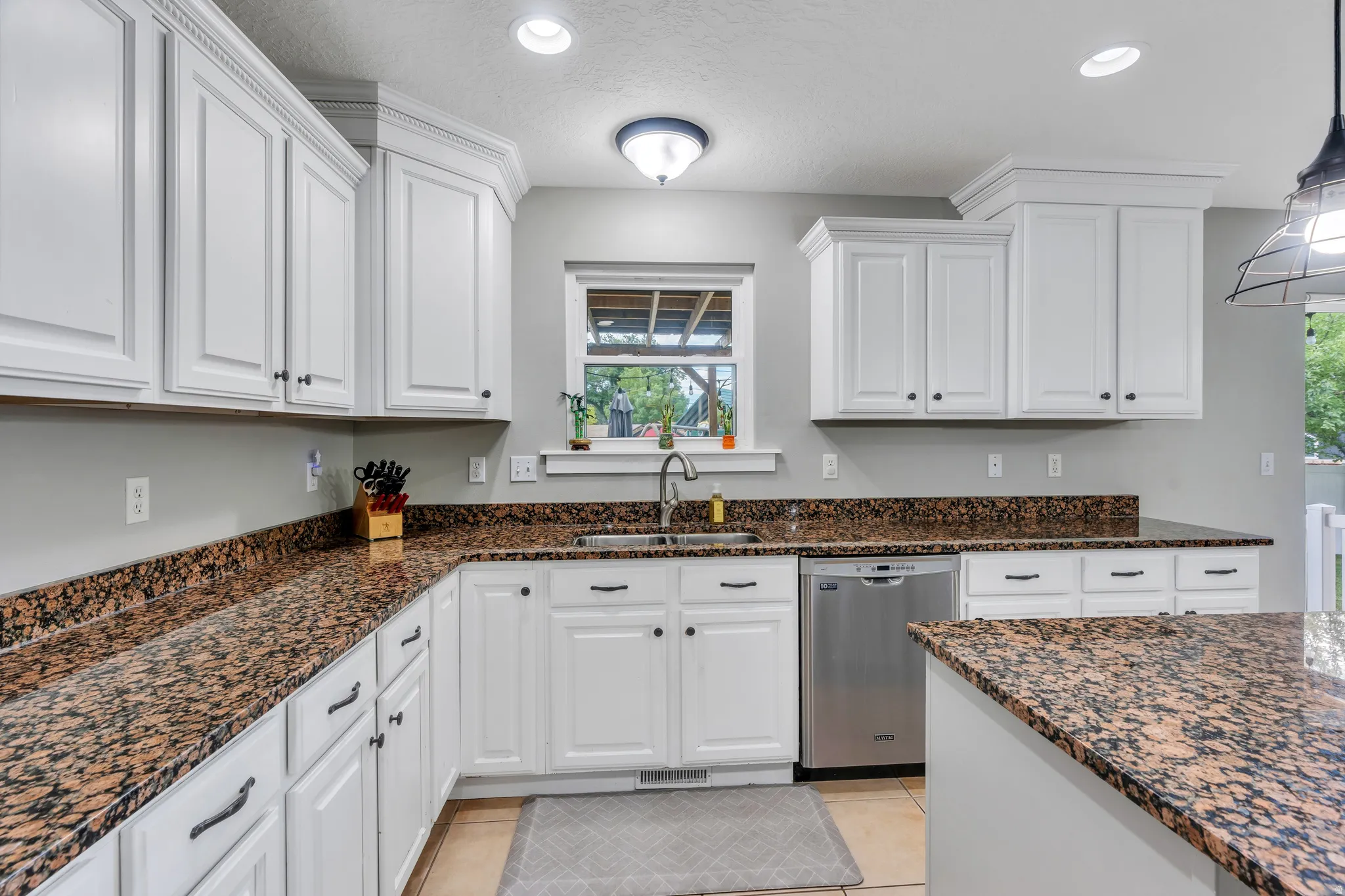 Kitchen featuring white cabinetry with dark hardware, brown granite countertops, a stainless steel dishwasher, an undermount sink, and recessed lighting