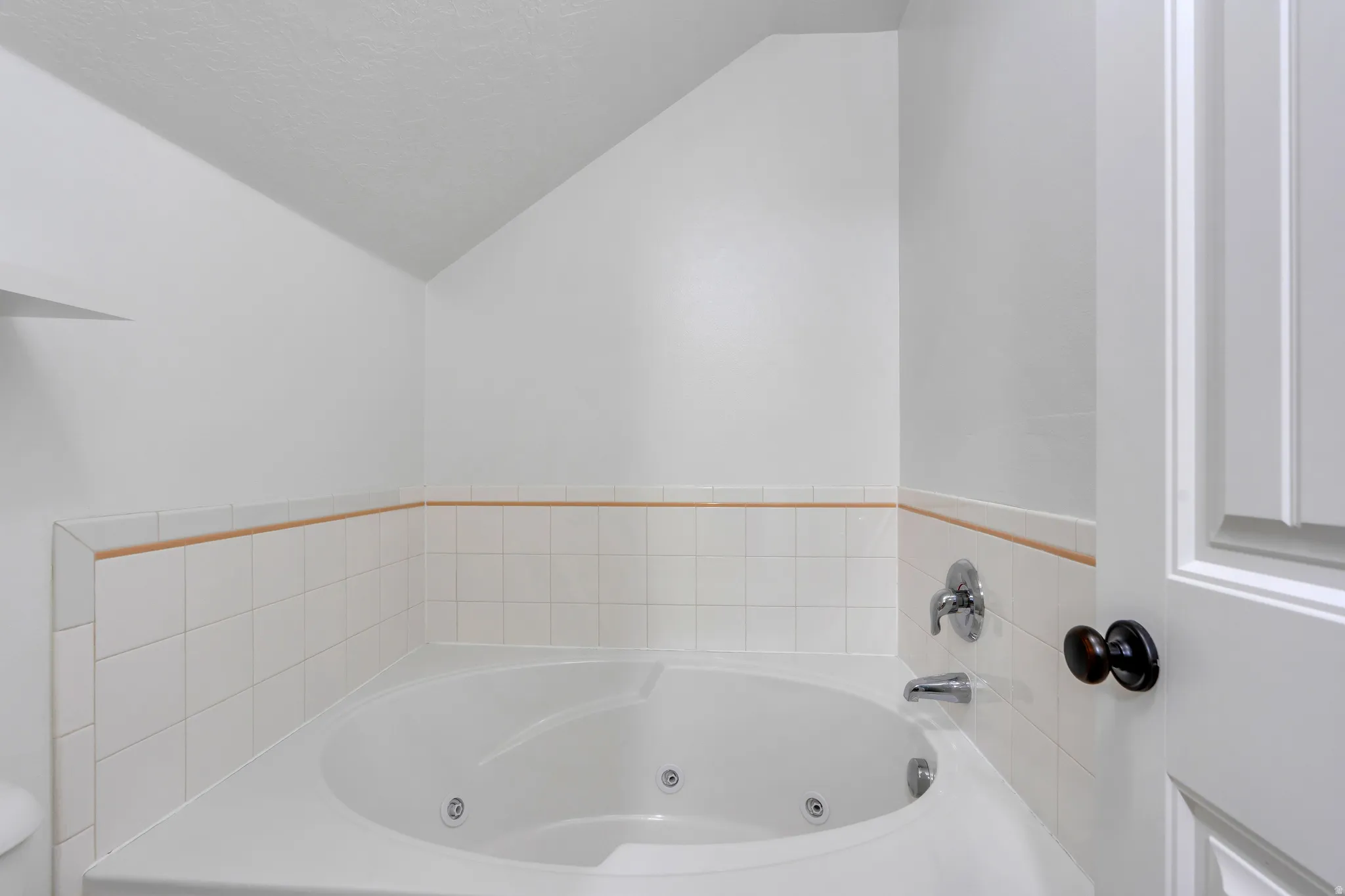 Corner jetted tub with white tile surround and integrated shelving