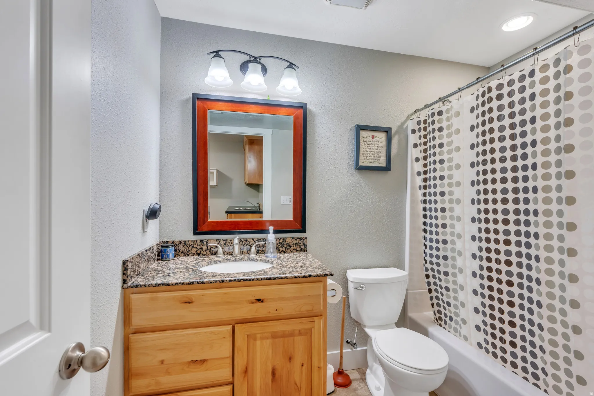 Bathroom featuring a wood vanity with a granite countertop, undermount sink, and a framed mirror