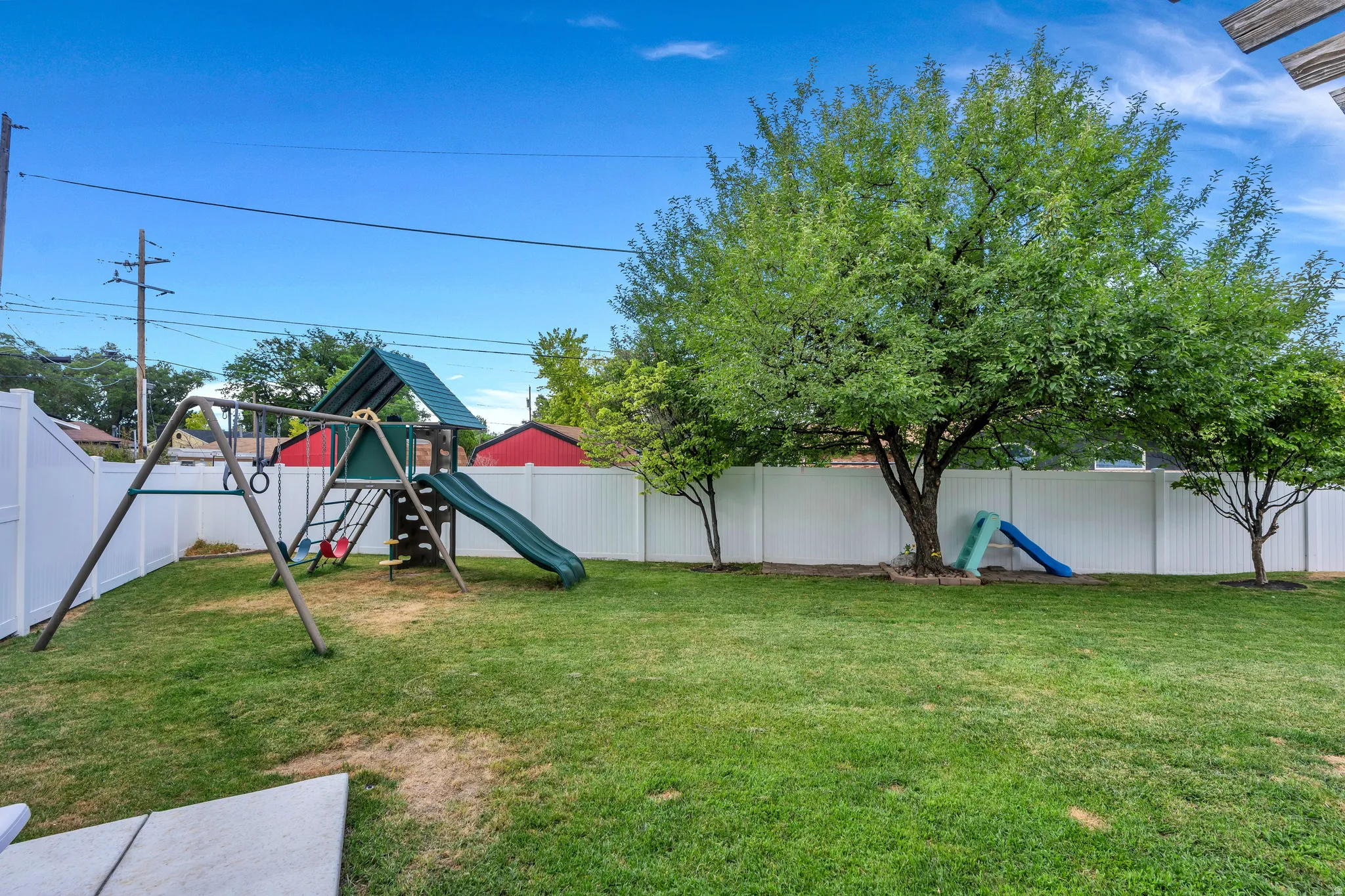 Expansive backyard featuring a large tree, a swing set, and a white privacy fence