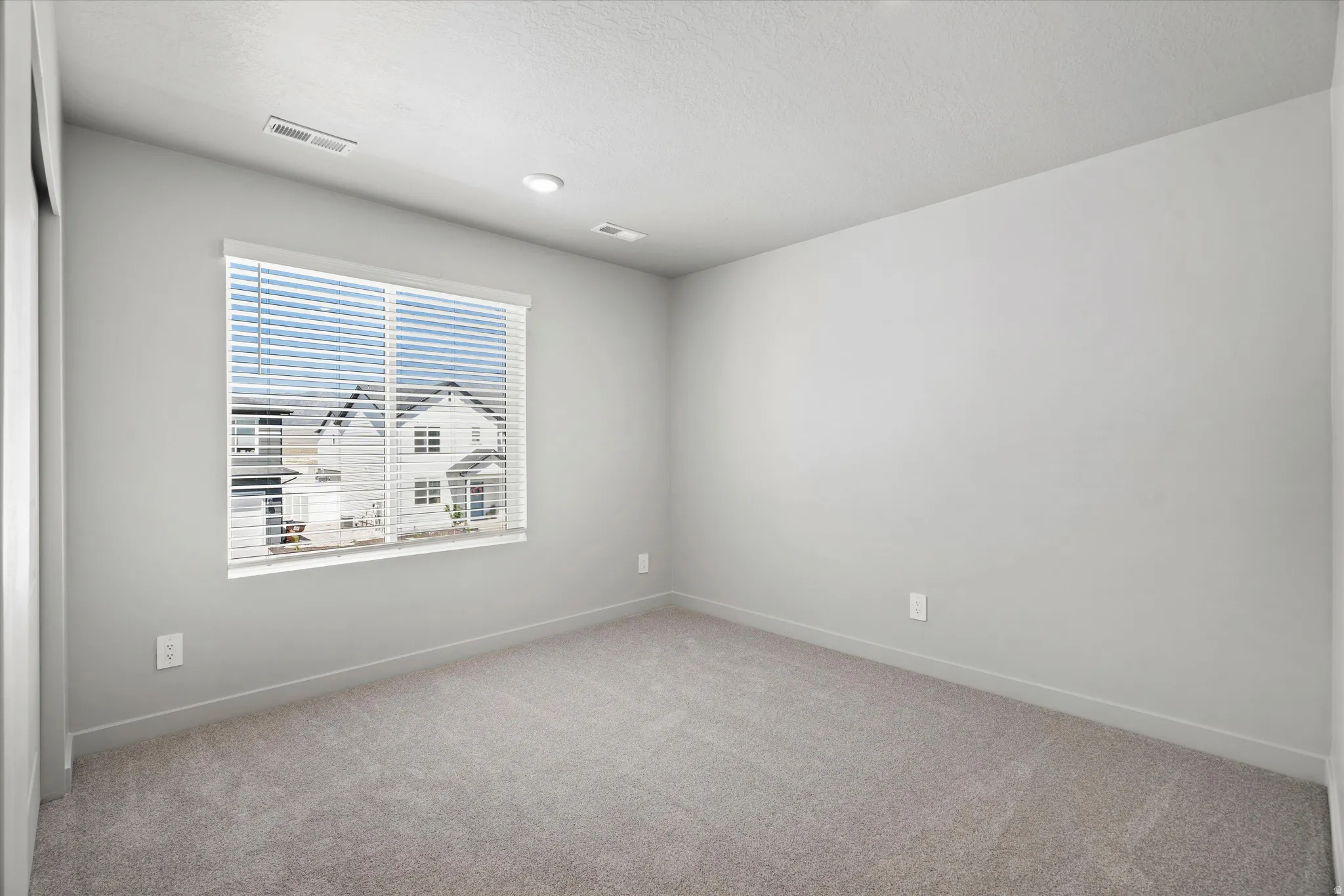Carpeted room featuring a large window with blinds, recessed lighting, and wall-mounted electrical outlets