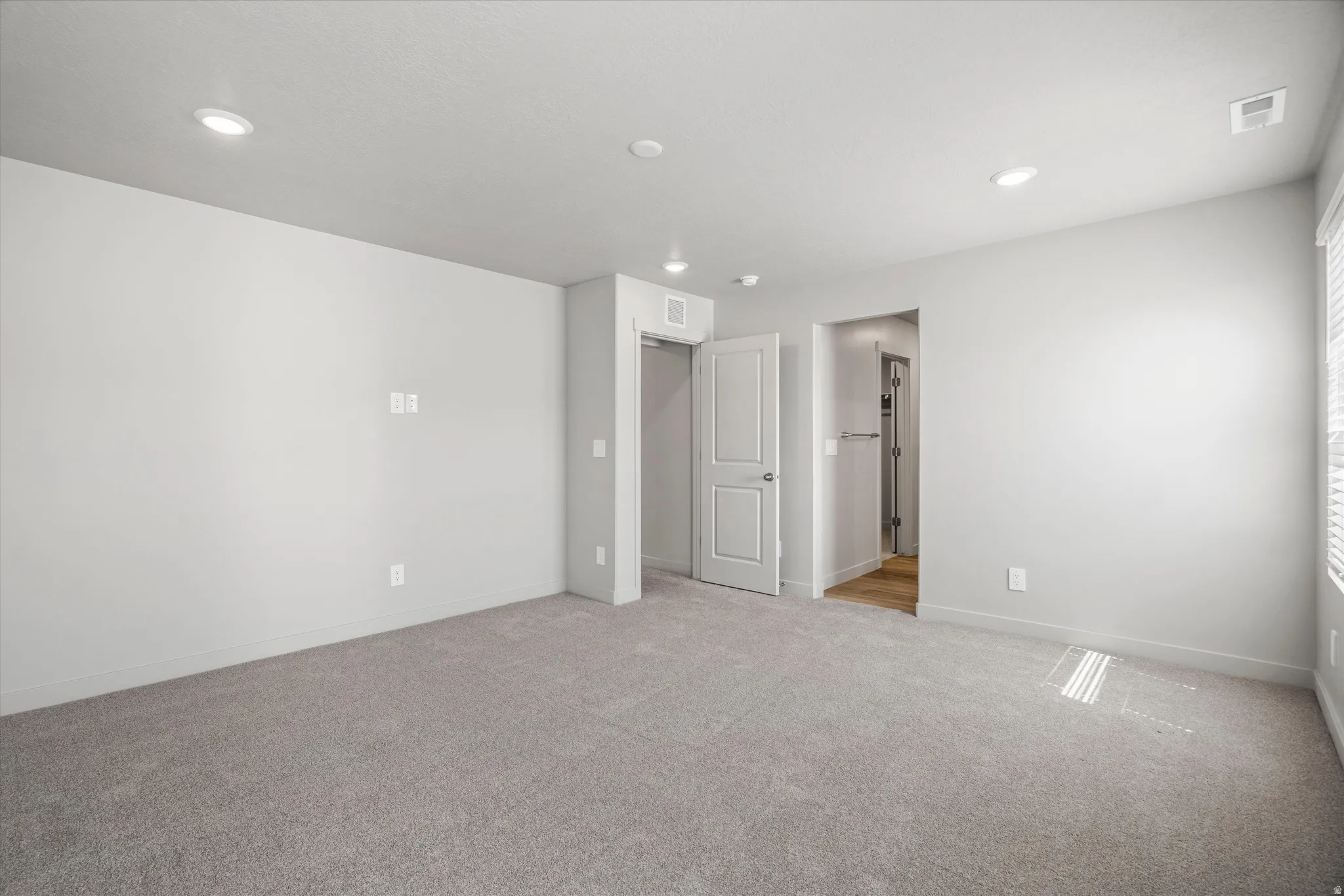Spacious room with gray carpeting, light gray walls, recessed lighting, and a window with blinds
