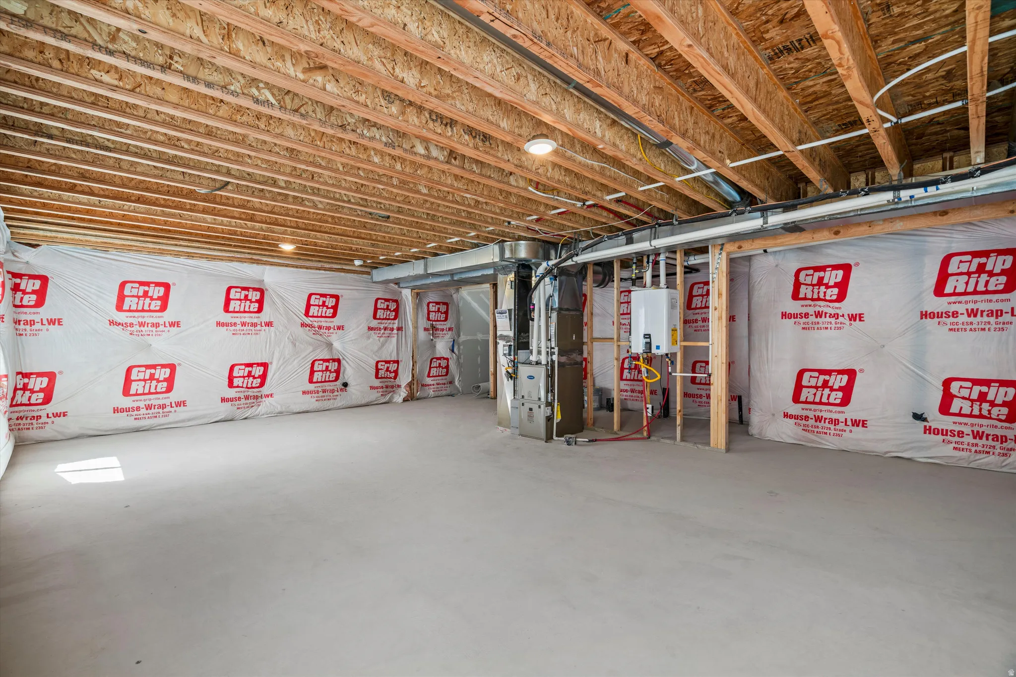 Unfinished basement space featuring exposed wood joists, house wrap insulation, and a concrete floor