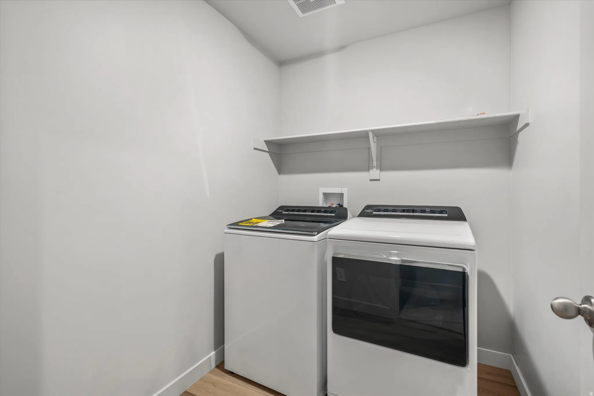 Dedicated laundry area featuring a white wall shelf, light wood-finish flooring, and a white baseboard