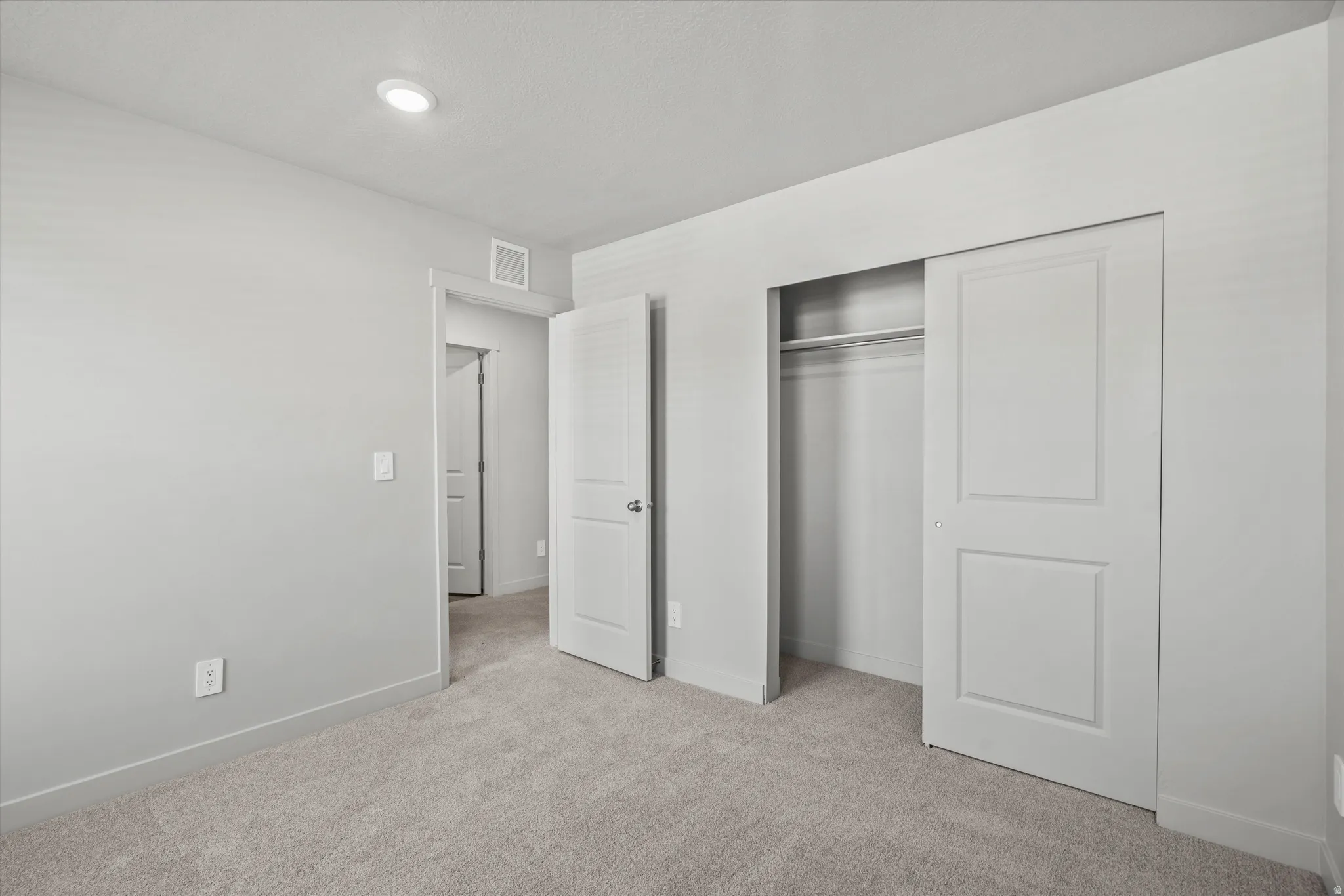 Bedroom featuring light gray walls, gray carpet, a recessed ceiling light, and a two-panel sliding closet door with interior hanging rod