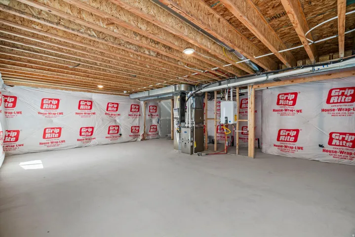 Unfinished basement space featuring exposed wood joists, house wrap insulation, and a concrete floor