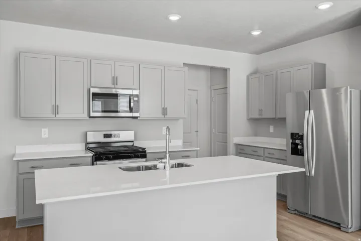 Kitchen featuring a central island with a double basin sink, stainless steel appliances, light gray cabinetry, solid surface countertops, and recessed lighting