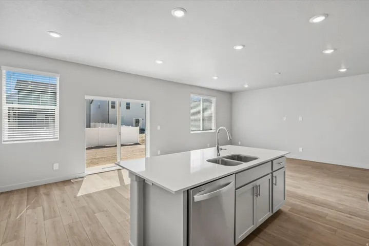 Kitchen island featuring a double-basin stainless steel sink with gooseneck faucet, light gray cabinetry, and a built-in dishwasher