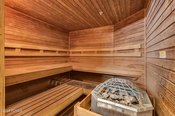 Dedicated sauna room featuring extensive wood paneling, multi-tiered wood bench seating, and an integrated sauna heater with stones