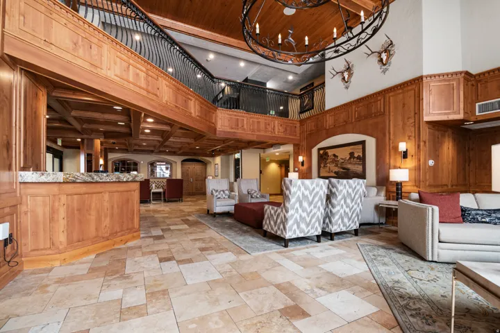 Expansive foyer featuring a grand staircase with wrought iron railing, intricate wood paneling, a large decorative chandelier, natural stone flooring, and a reception counter with a stone surface