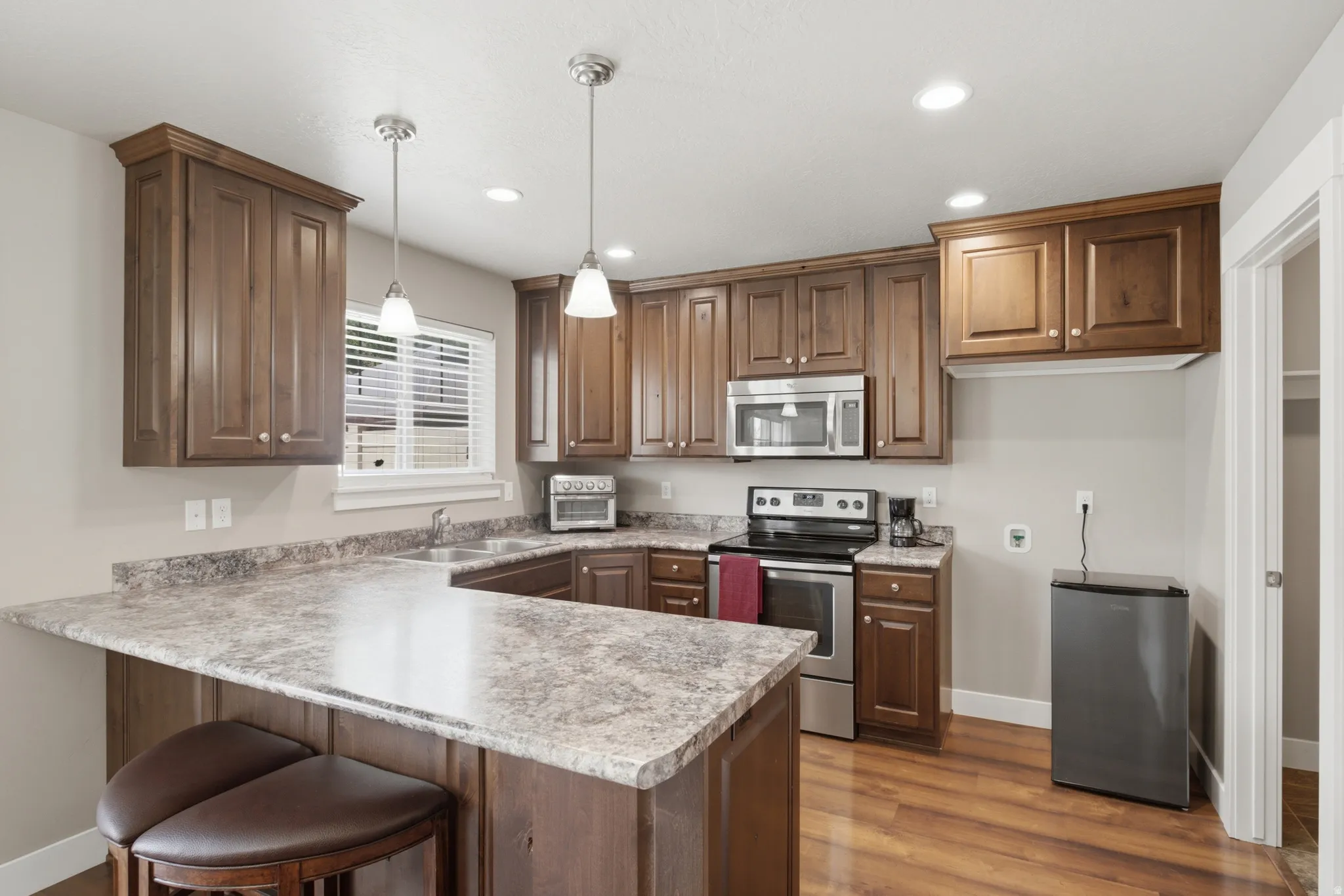 Kitchen featuring wood-finish flooring, abundant cabinetry, stone-look countertops, and stainless steel appliances