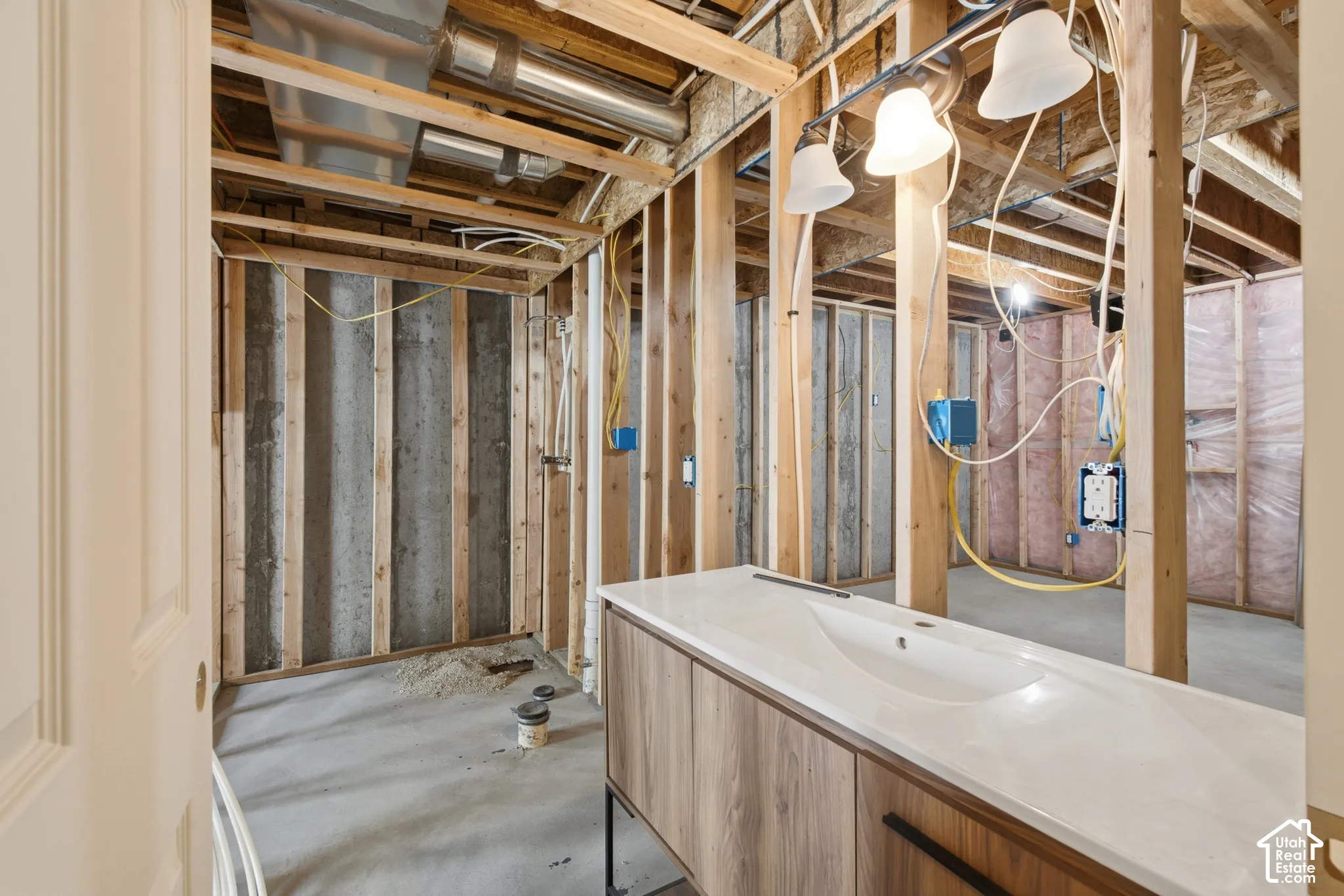 Unfinished basement space featuring exposed wooden framing, concrete flooring, visible HVAC ductwork, electrical wiring, and a built-in vanity with an integrated sink