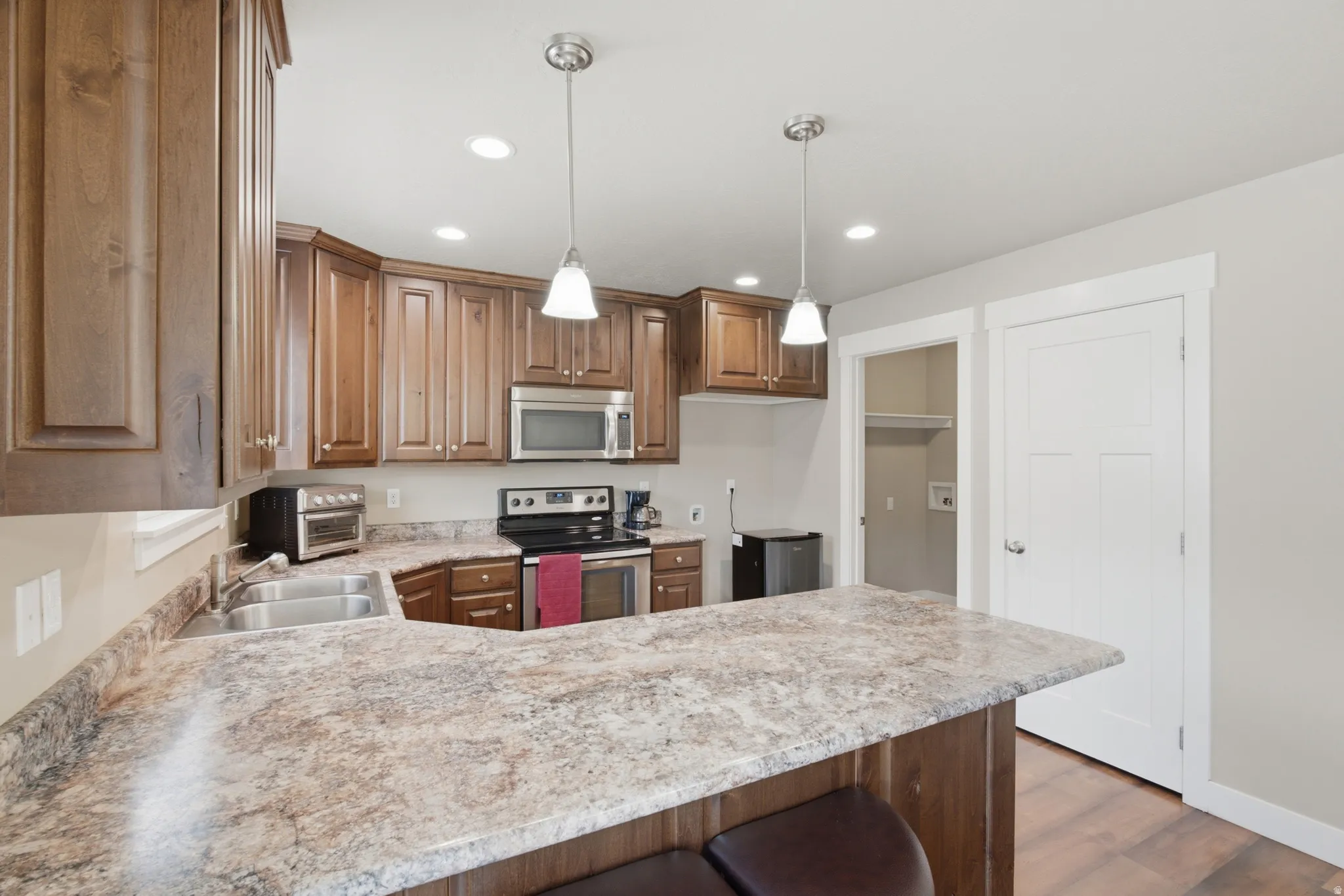 Kitchen featuring wood cabinetry, stainless steel appliances, a double basin sink, and pendant lighting
