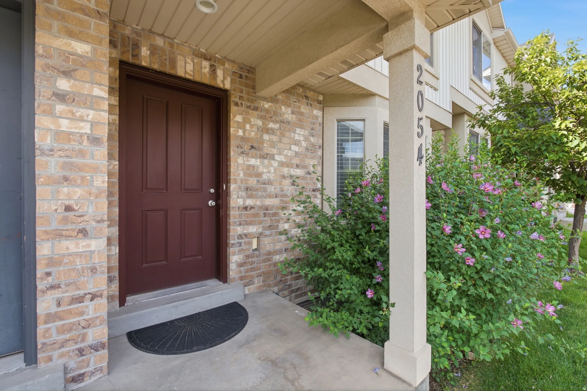 Brick exterior facade featuring a paneled entry door, concrete porch, and bay windows