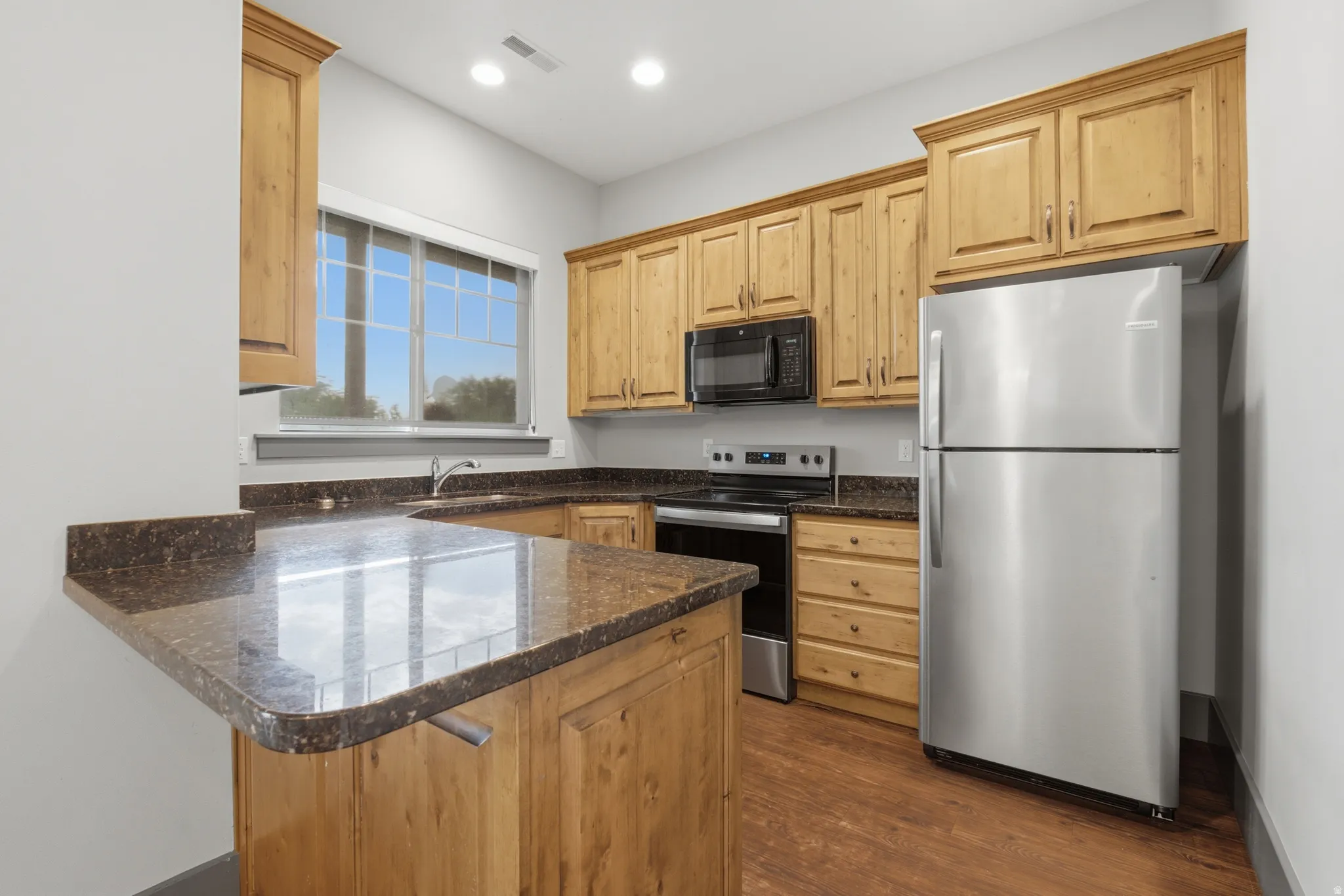 Kitchen featuring wood cabinetry, dark granite-style countertops, and stainless steel appliances including a refrigerator, range, and microwave