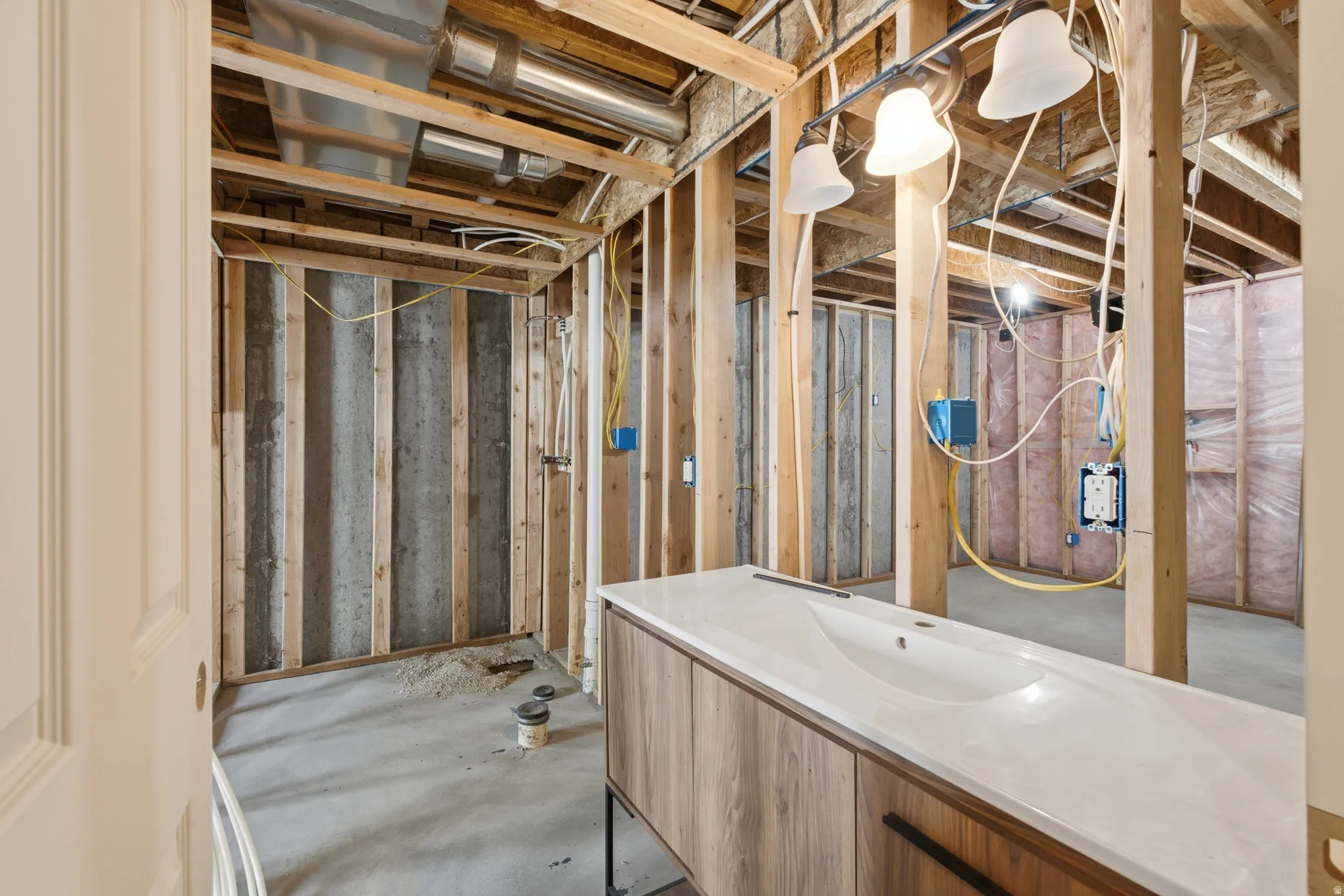 Unfinished basement space featuring exposed wooden framing, concrete flooring, visible HVAC ductwork, electrical wiring, and a built-in vanity with an integrated sink