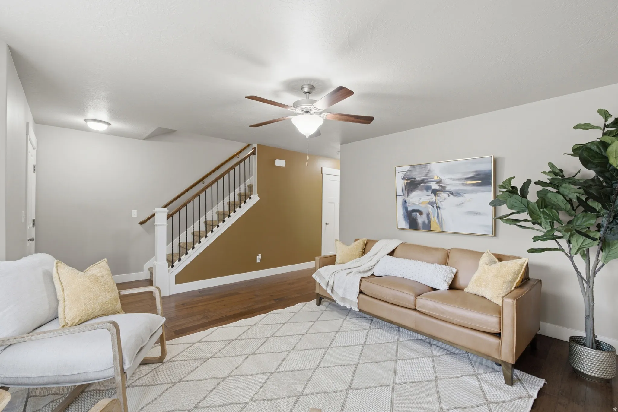Living area featuring wood-finish flooring, a ceiling fan with integrated lighting, and a staircase with white risers and dark wood handrail