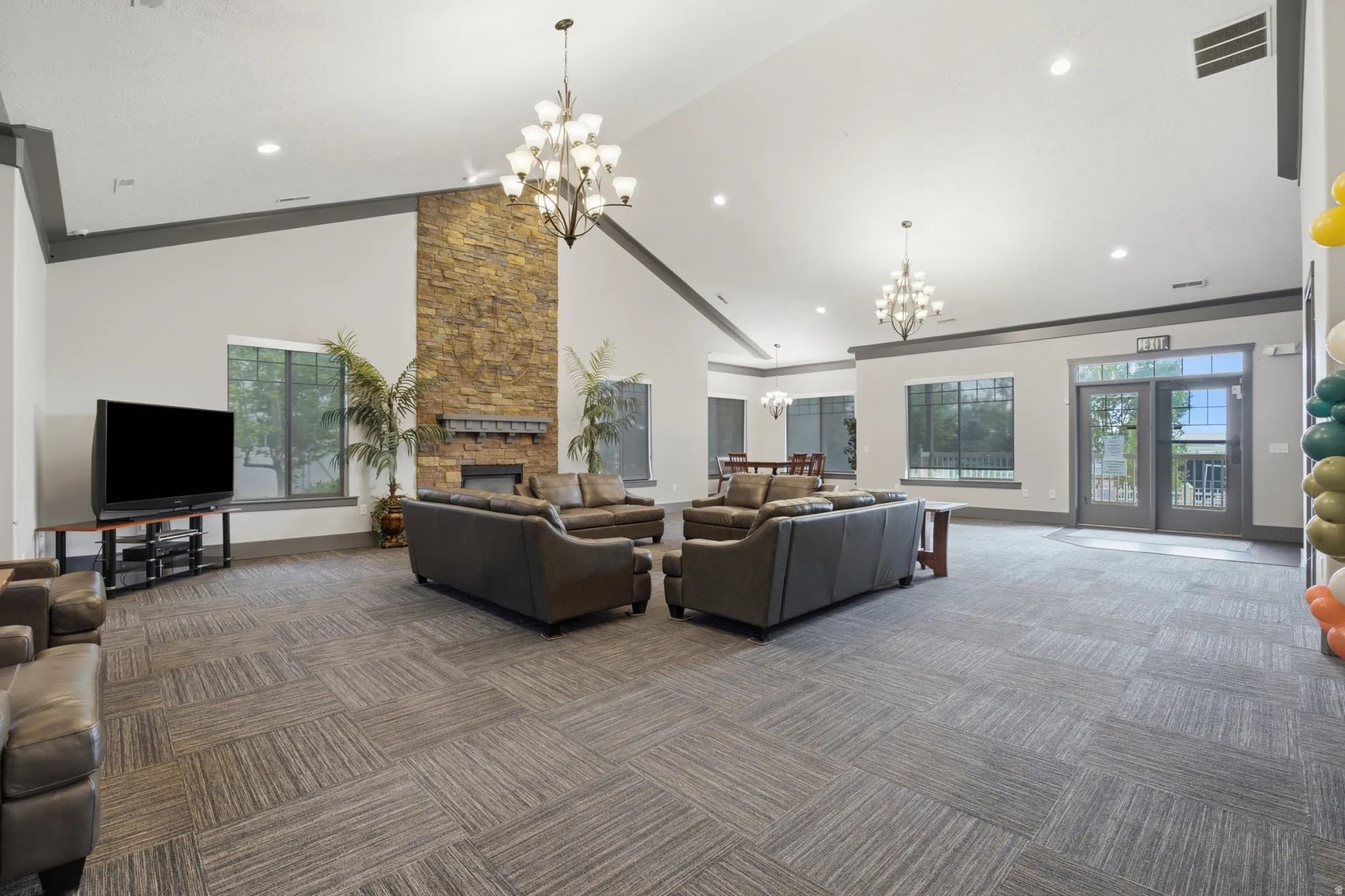 Spacious common area featuring a stone-clad fireplace, vaulted ceilings, and large windows