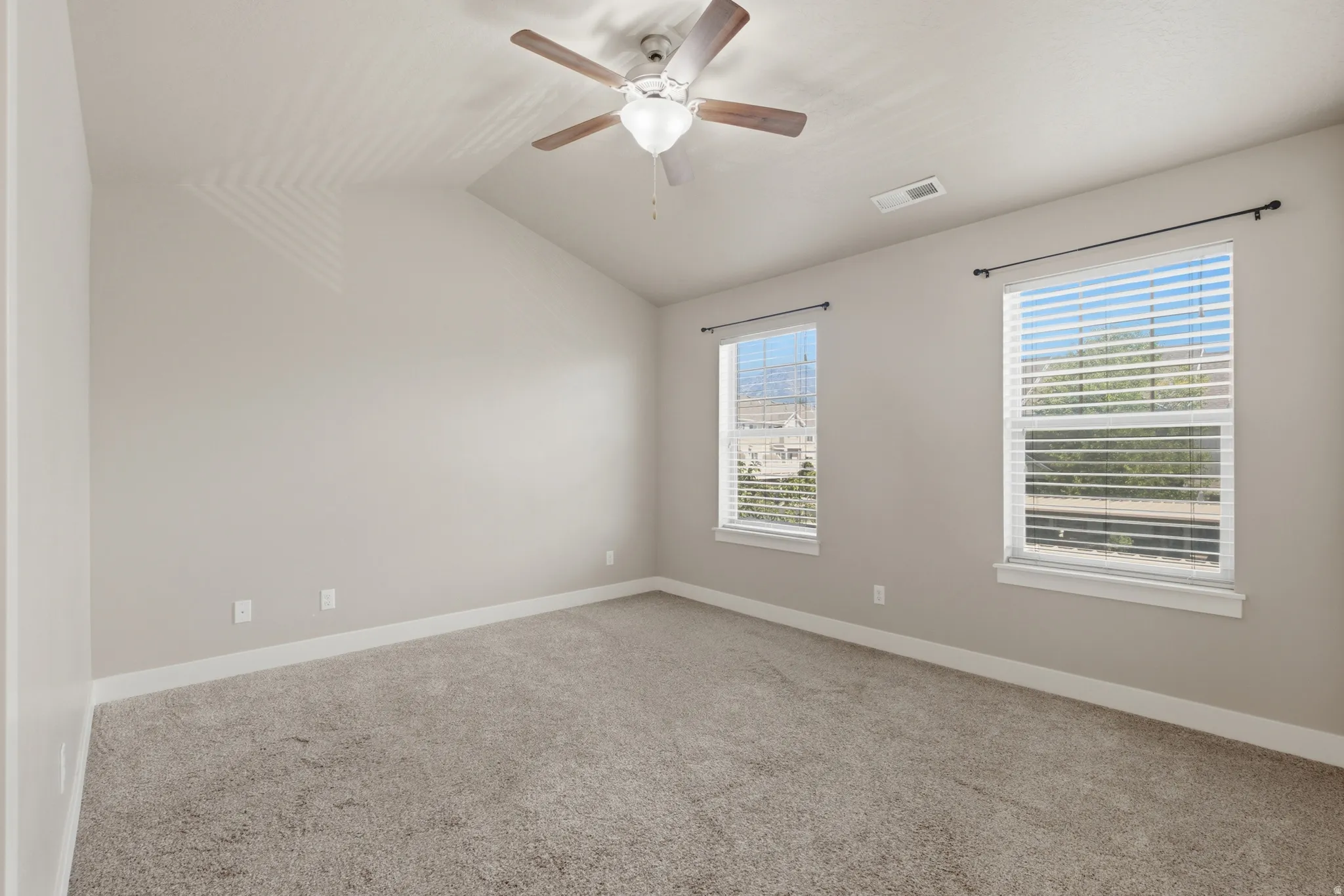 Spacious room featuring vaulted ceilings, light gray wall paint, and gray carpet flooring