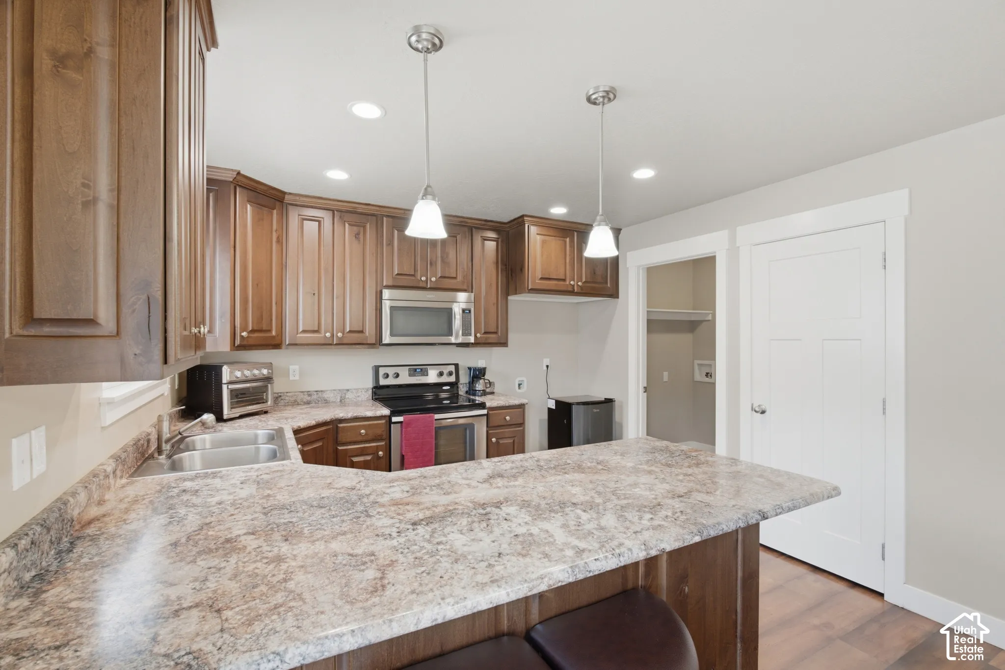 Kitchen featuring wood cabinetry, stainless steel appliances, a double basin sink, and pendant lighting