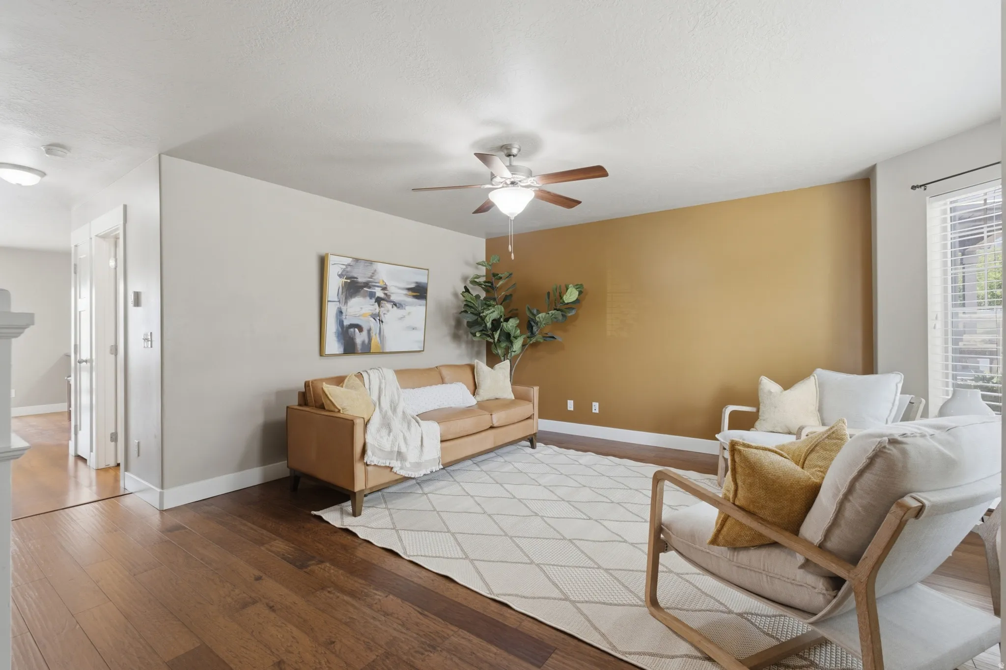 Spacious living area featuring wood-finish flooring, a ceiling fan with integrated lighting, and a window with horizontal blinds
