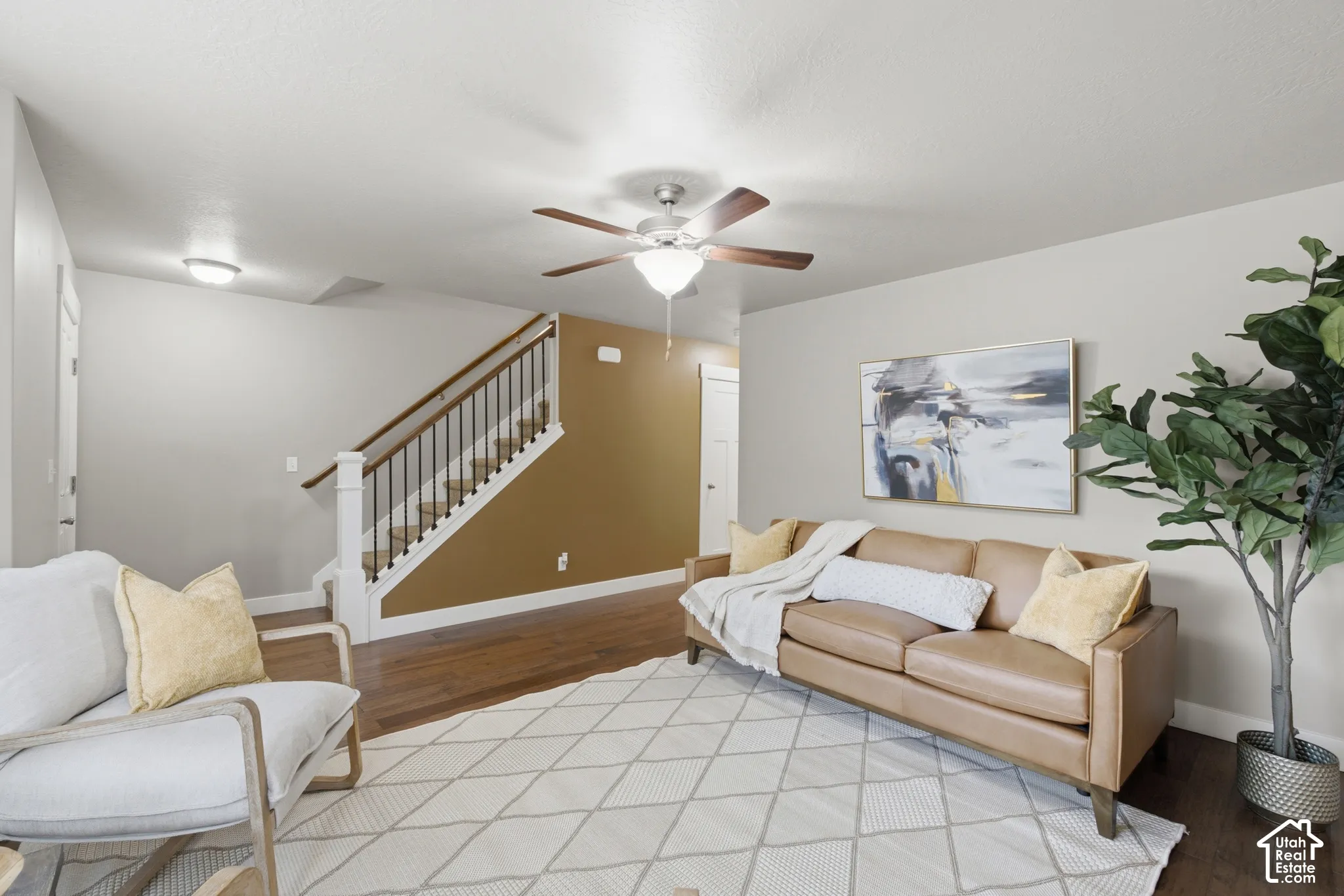 Living area featuring wood-finish flooring, a ceiling fan with integrated lighting, and a staircase with white risers and dark wood handrail