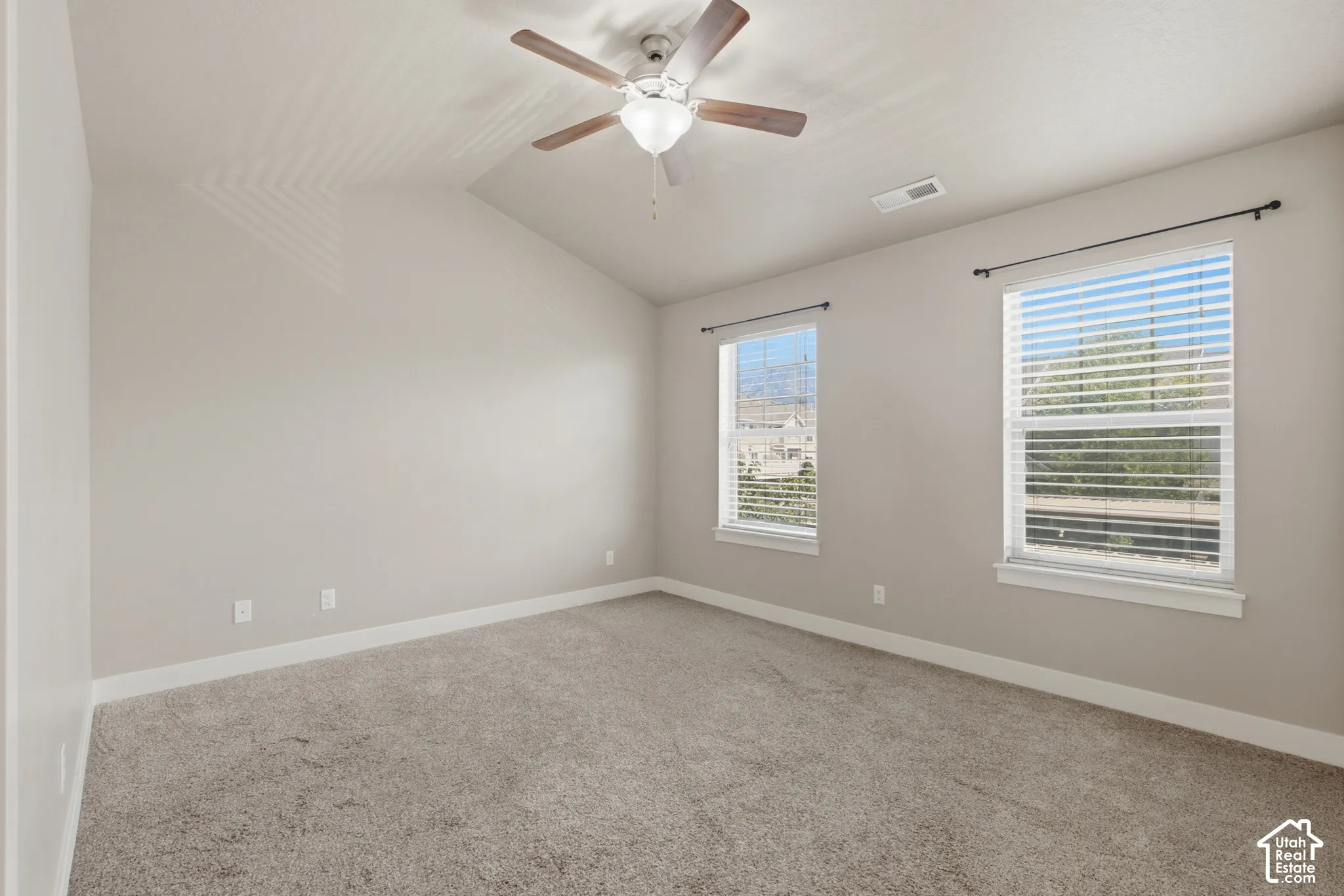 Spacious room featuring vaulted ceilings, light gray wall paint, and gray carpet flooring