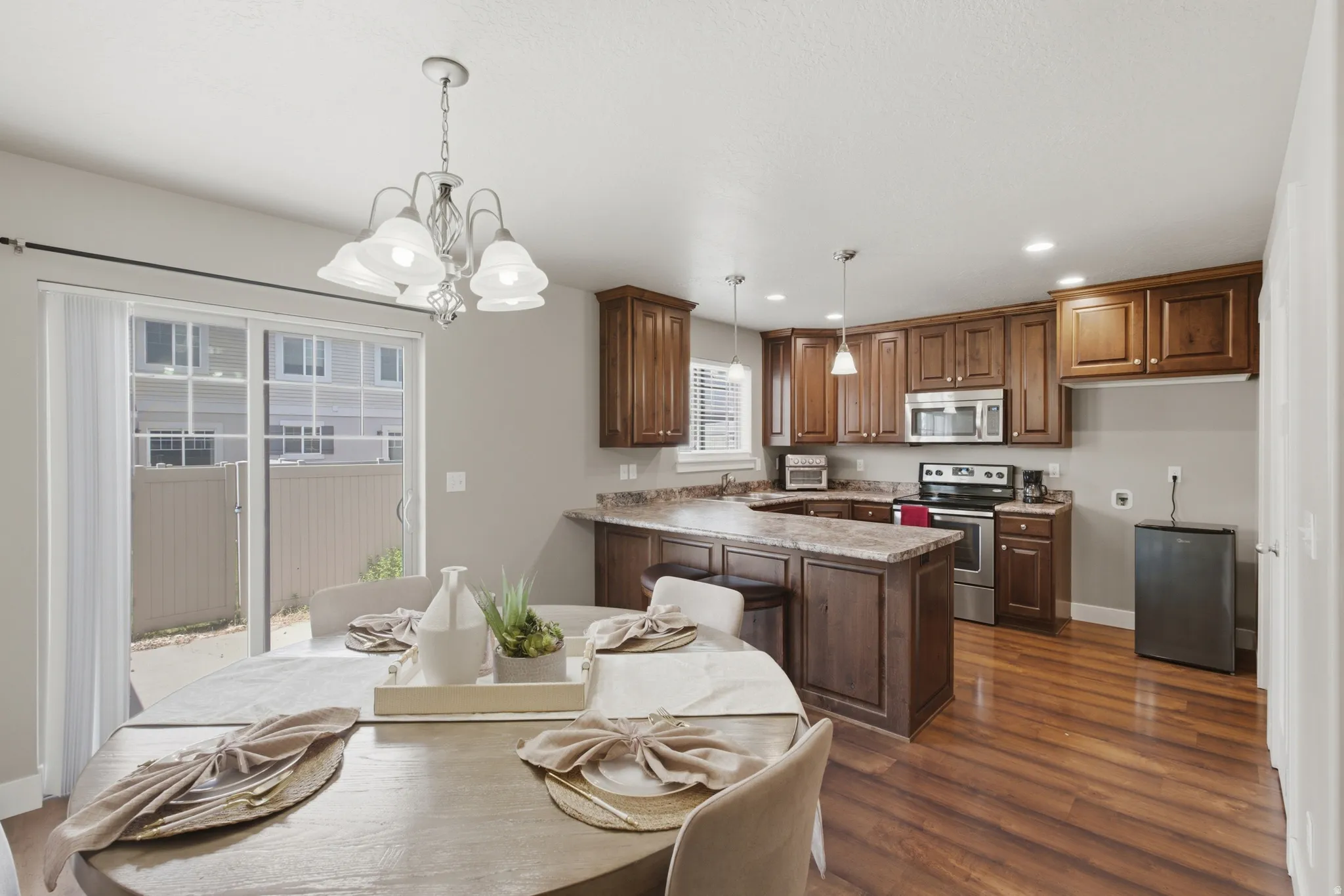 Open-concept kitchen and dining area featuring wood-finish flooring, rich wood cabinetry, stainless steel appliances, and a breakfast bar with stone-finish countertops