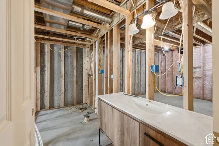 Unfinished basement space featuring exposed wooden framing, concrete flooring, visible HVAC ductwork, electrical wiring, and a built-in vanity with an integrated sink