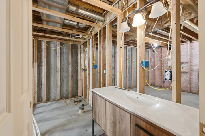 Unfinished basement space featuring exposed wooden framing, concrete flooring, visible HVAC ductwork, electrical wiring, and a built-in vanity with an integrated sink