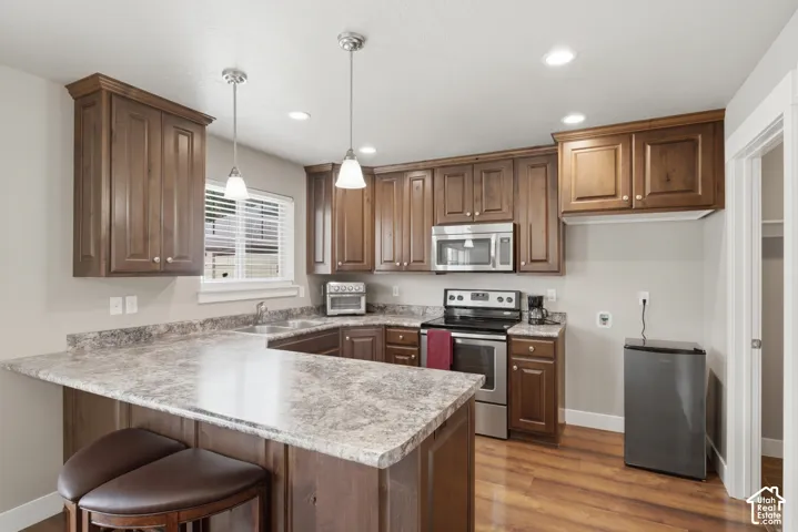 Kitchen featuring wood-finish flooring, abundant cabinetry, stone-look countertops, and stainless steel appliances