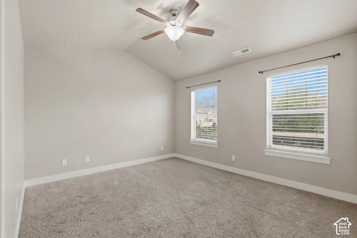 Spacious room featuring vaulted ceilings, light gray wall paint, and gray carpet flooring