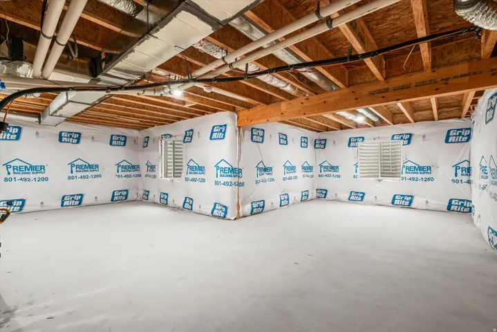 Unfinished basement featuring exposed wood joists and subflooring, insulated walls, concrete flooring, and multiple window wells