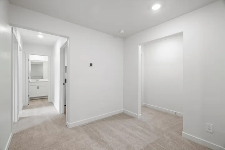 Bright interior space featuring light-colored carpeting, white baseboards, and doorways leading to other areas