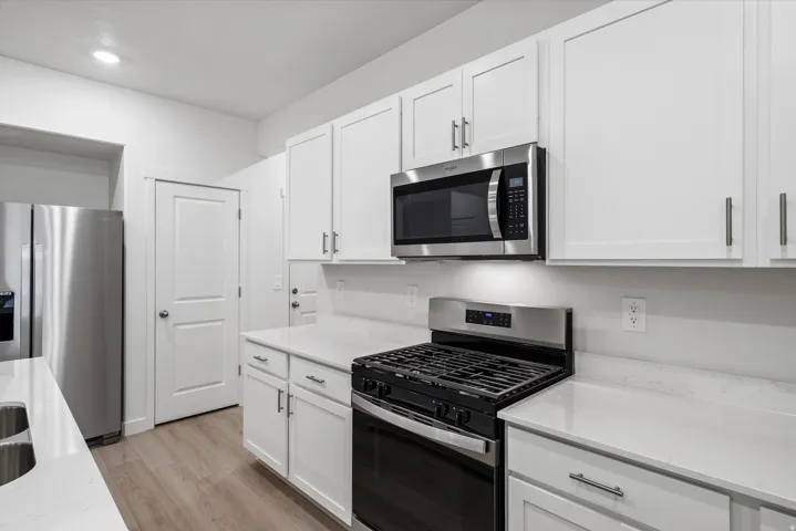 Modern kitchen featuring white shaker cabinetry, stainless steel appliances, light-toned countertops, and wood-finish flooring