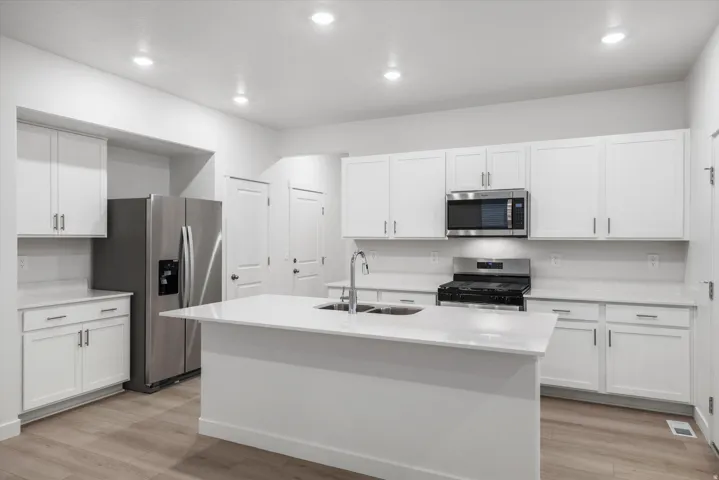 Contemporary kitchen featuring a large central island with an undermount sink, white cabinetry, integrated stainless steel appliances, light-toned countertops, and wood-finish flooring
