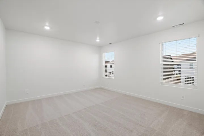 Spacious room featuring neutral carpet flooring, recessed lighting, and two windows with blinds