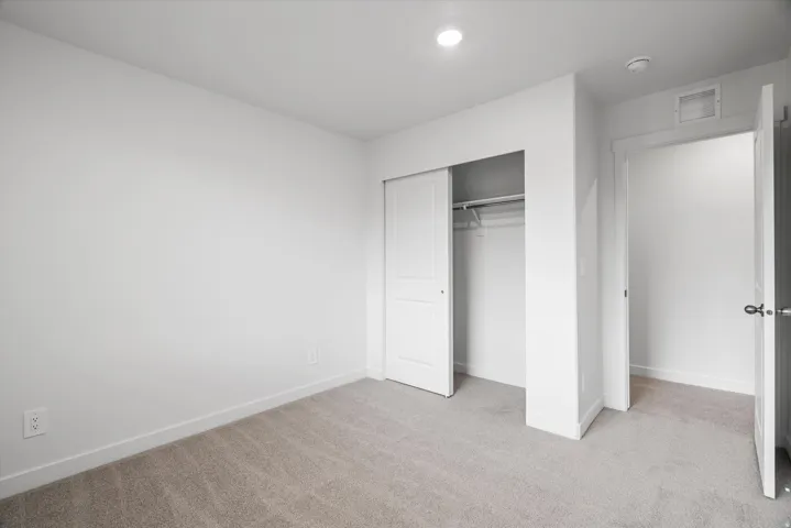 Neutral tone wall paint, light gray carpet flooring, recessed ceiling lighting, and a sliding door closet with an interior hanging rod