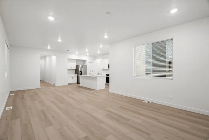 Open-concept living area with wood-finish flooring, recessed lighting, and a window with blinds