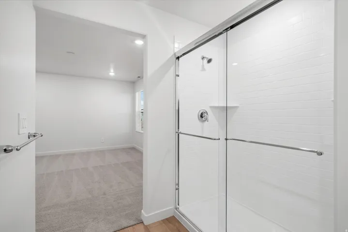 Shower stall with glass enclosure and white subway tile surround, featuring chrome fixtures and a built-in shelf