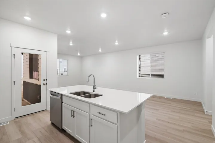 Open-concept kitchen and living area featuring a central island with white cabinetry, a dual basin sink, and a stainless steel dishwasher